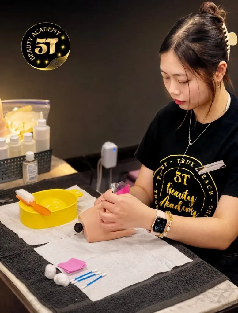 Nail technician student practicing professional manicure and nail care techniques during hands-on training at 5T Beauty Academy.